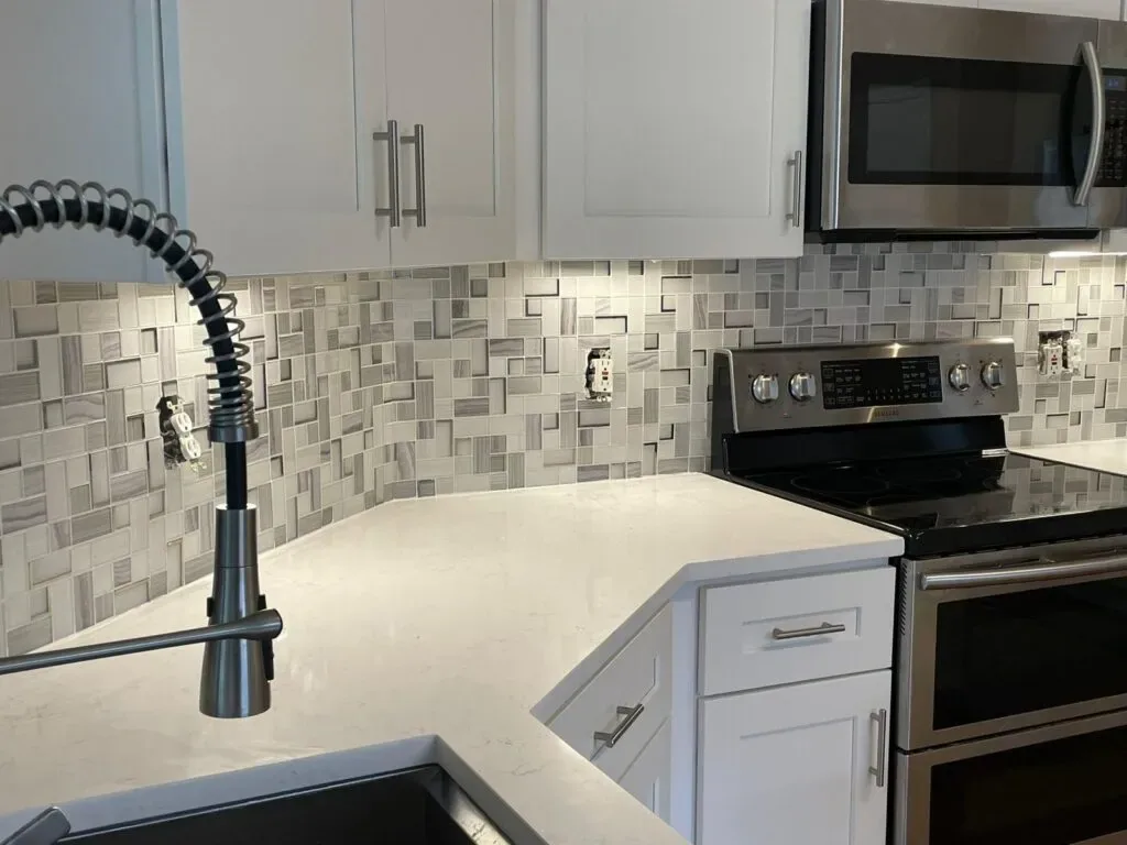 Renovated kitchen corner with white cabinetry, geometric backsplash, and work lighting